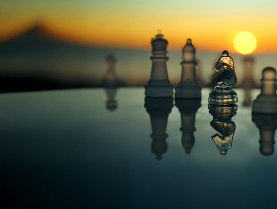 A game of chess with a beautiful glass chess set at sunrise by the sea. The knight is featured.
