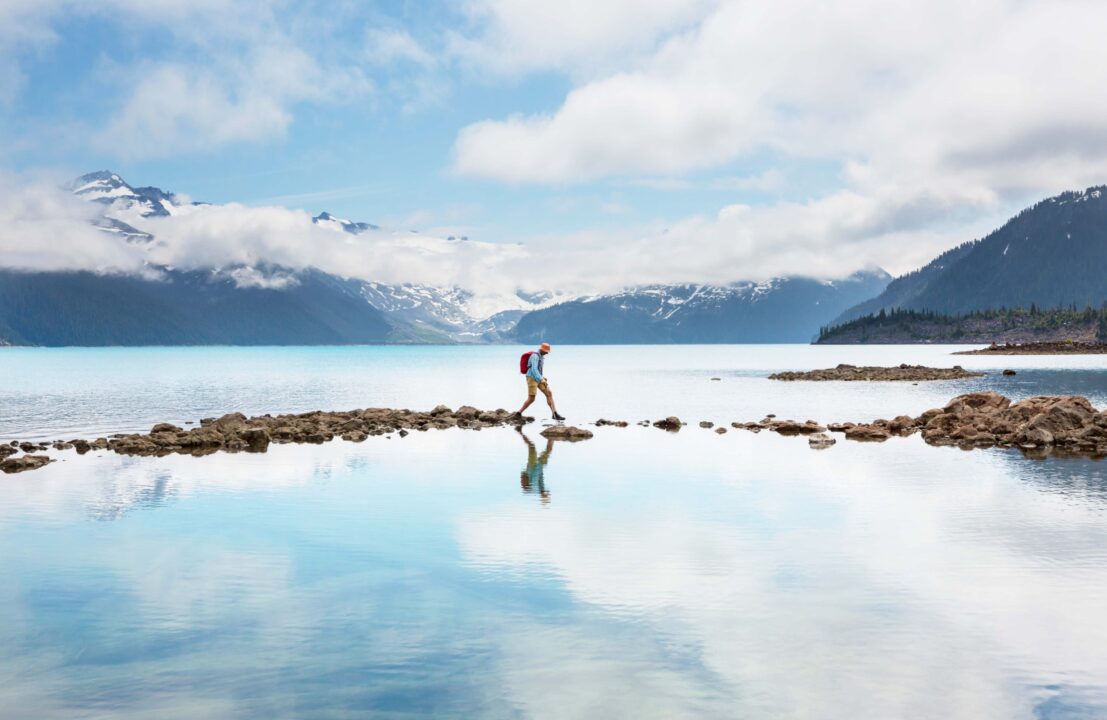 Person walking on the beach with clouds reflected in water