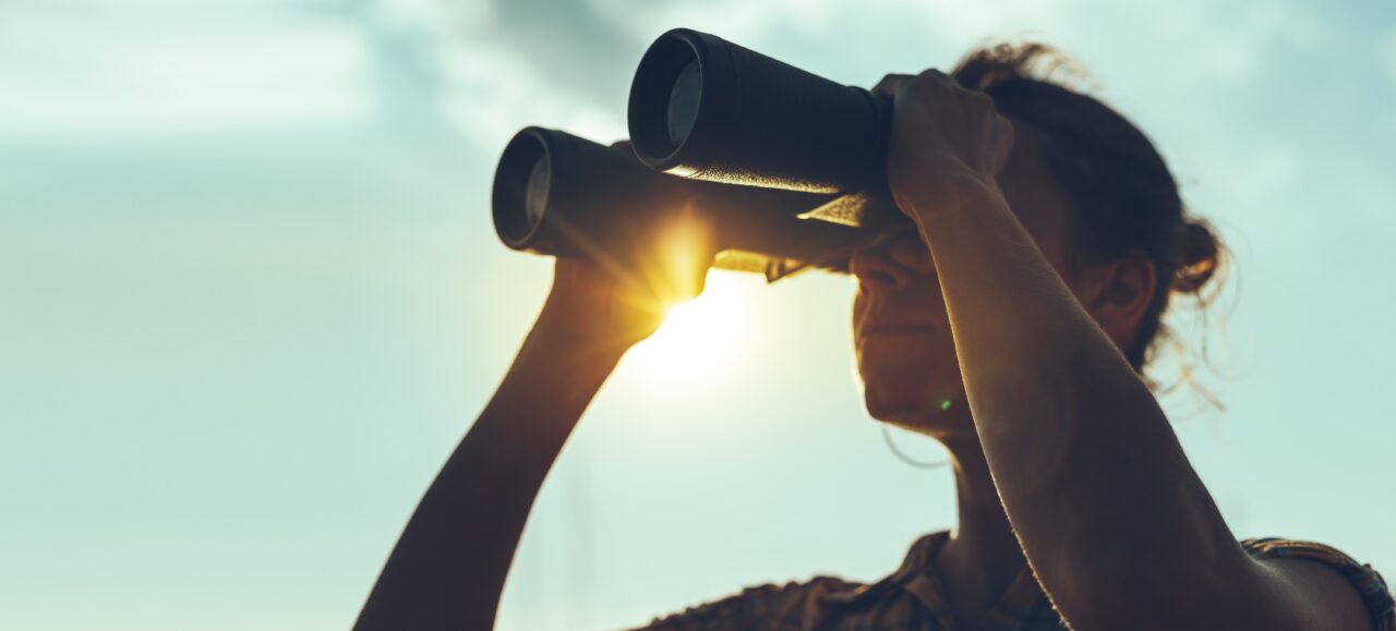 Woman in shadow looking through binoculars with the sun in the background