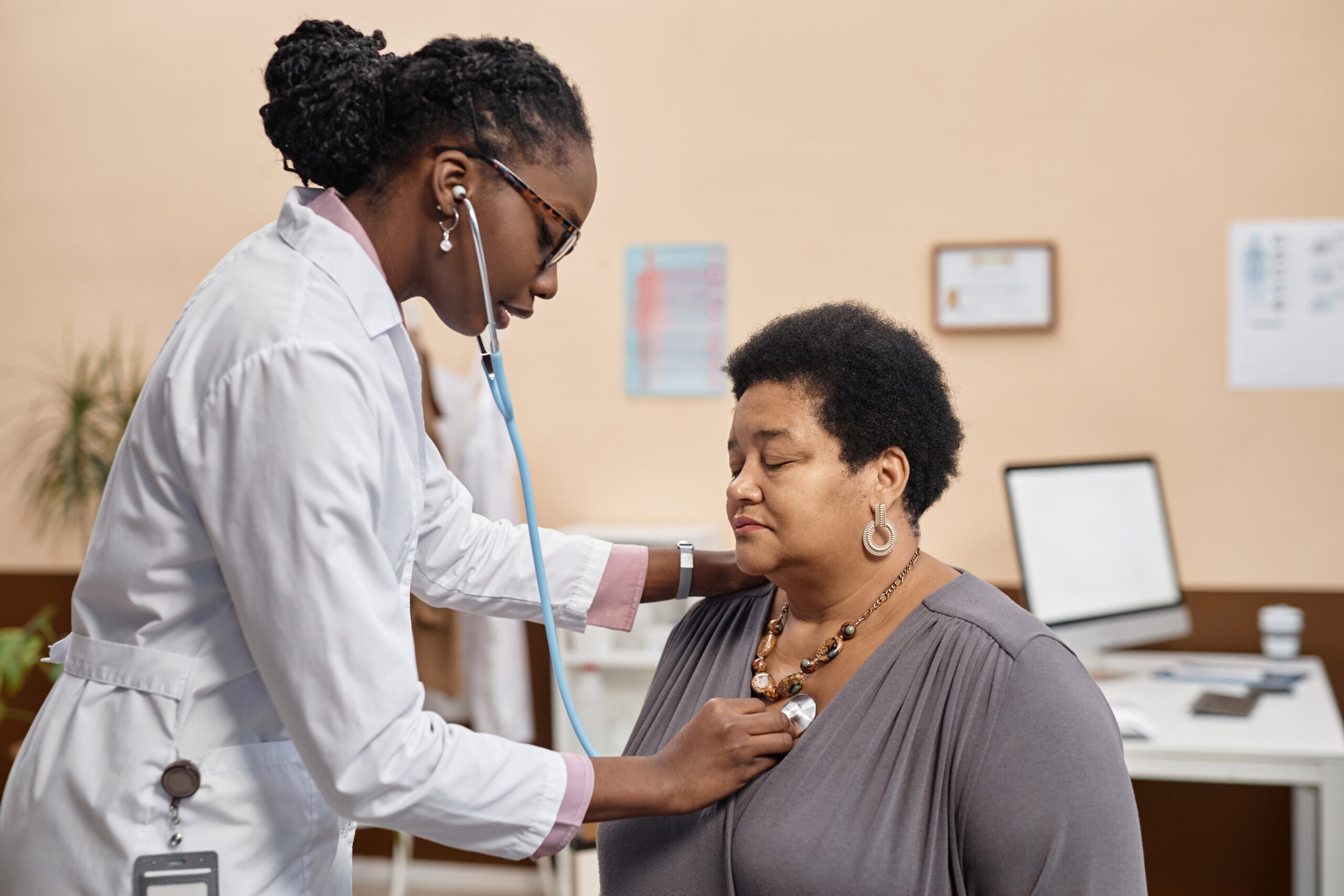 Female physician using stethoscope while asking senior female patient to make a deep breath during medical examination