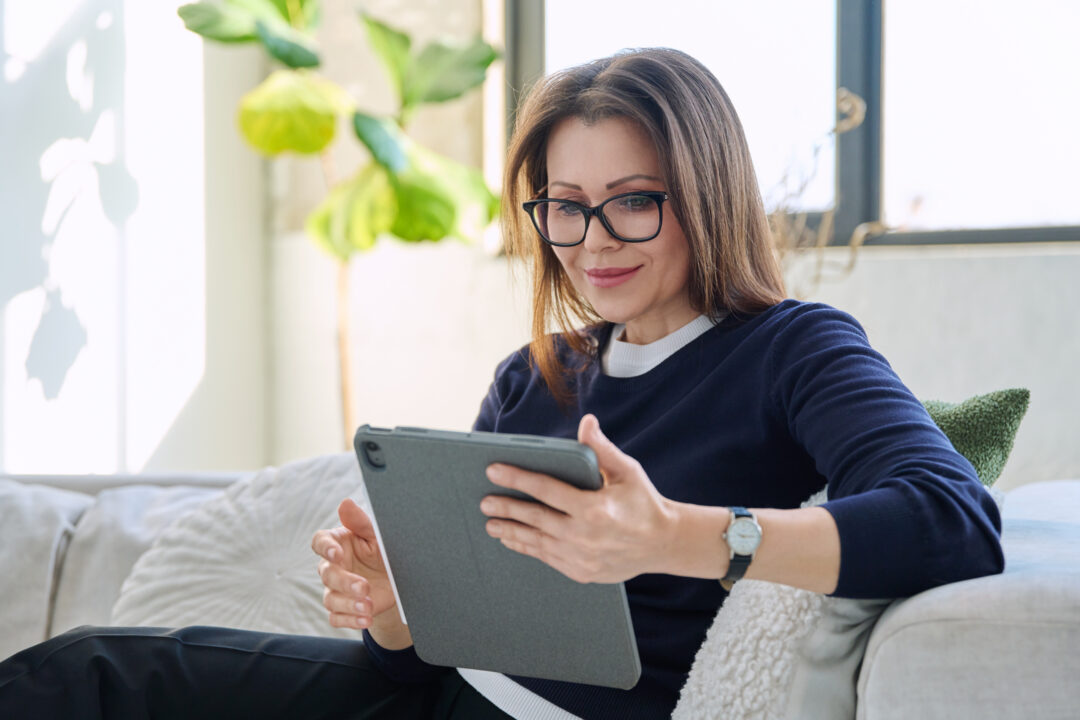 Woman looking at digital tablet sitting on sofa at home